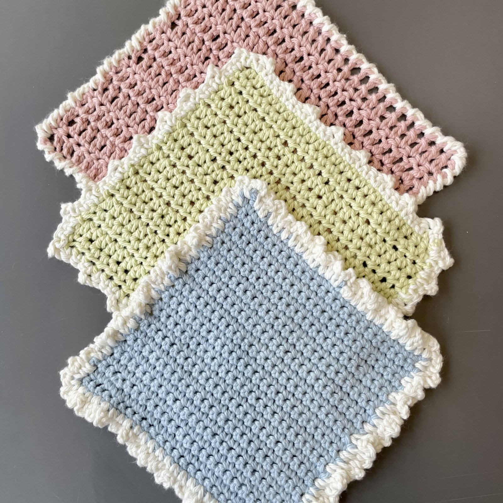 Three crocheted dishcloths with white crochet borders.