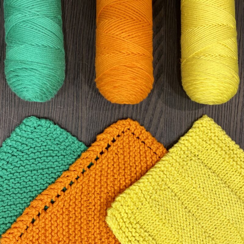 Three colors of yarn and three knit dishcloths demonstrating learning to knit.